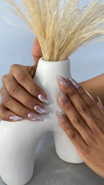 Uñas cromadas lila junto a un jarrón blanco