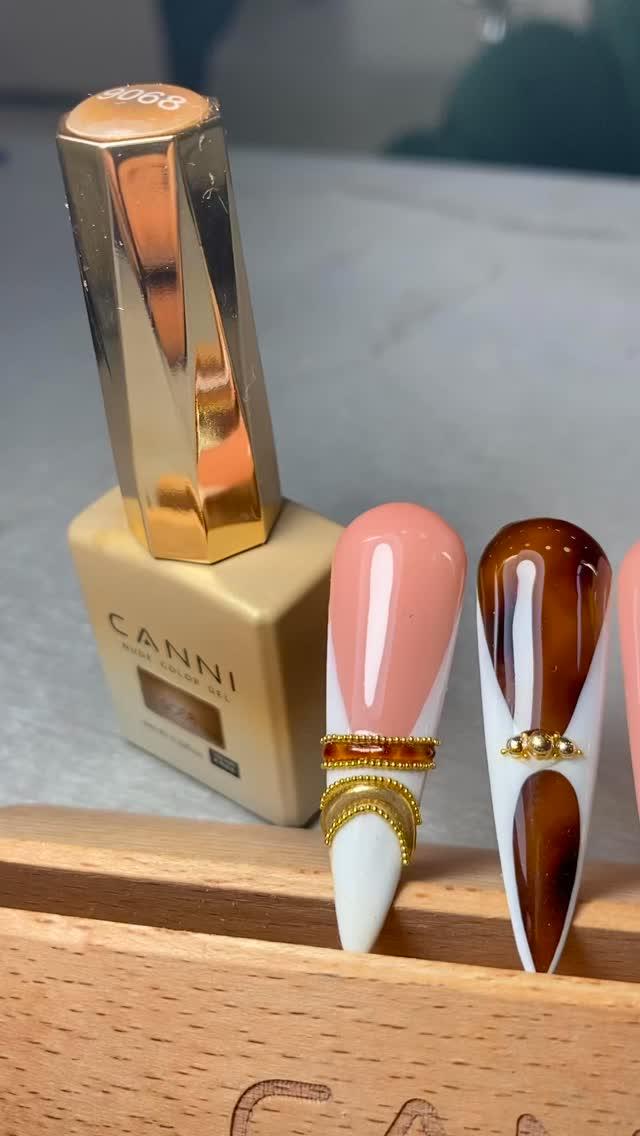 Frasco de gel dorado junto a dos uñas stiletto de muestra